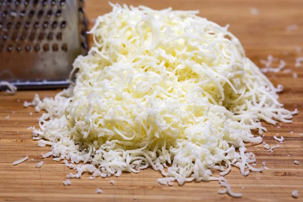 Queso mozzarella rallado en una tabla de cortar con un rallador —  Fotos de Stock