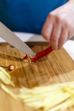 Adam mutfaktaki ahşap bir keresteyle sebze kesiyor.