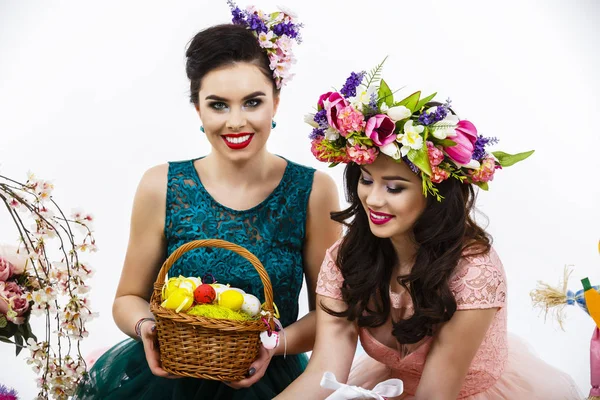 Dvě krásné přítelkyně holky, košík s vejci a dekorativní květina — Stock fotografie