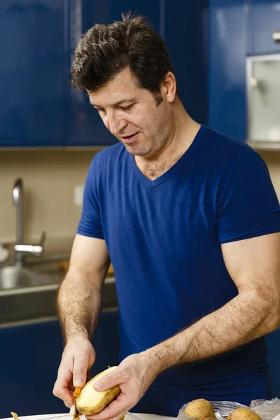 Muž loupání brambor na pultě v kuchyni — Stock fotografie