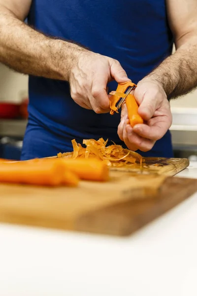 Человек чистит морковь на деревянной доске — стоковое фото