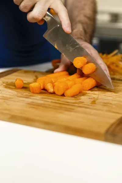 Τα χέρια του σεφ κοπή καθαρισμένα καρότα σε ένα ξύλινο ταμπλό με — Φωτογραφία Αρχείου
