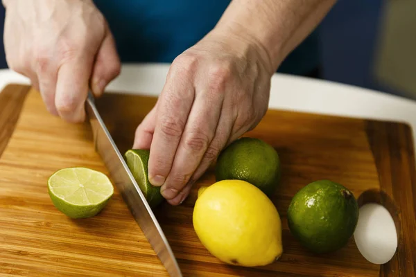 Hombre rebanando limas y limones en una tabla de madera — Foto de Stock