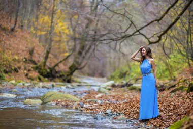 Sonbahar günü nehrin kenarında mavi elbiseli bir kadın.