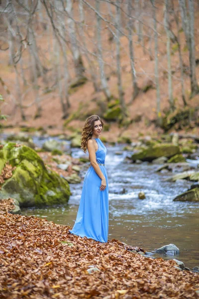 Kvinna i blå klänning nära en flod på höstdagen — Stockfoto