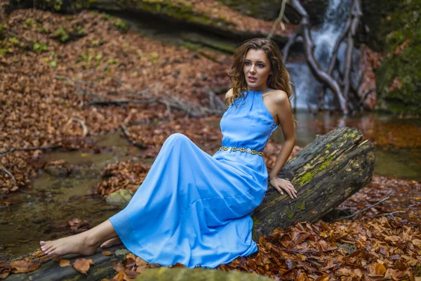 Eine schöne Frau im blauen Kleid in der Nähe eines Wasserfalls an einem Herbsttag — Stockfoto