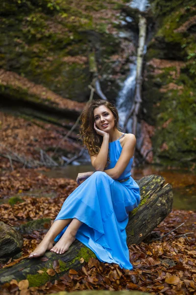 Une belle femme en robe bleue près d'une cascade le jour d'automne — Photo