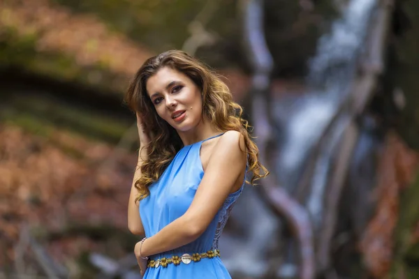 Piękna kobieta w niebieskiej sukience w pobliżu wodospadu w jesienny dzień — Zdjęcie stockowe