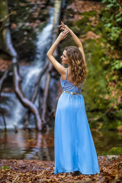 Красива жінка в синій сукні біля водоспаду в осінній день — стокове фото