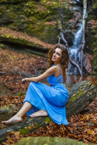 Eine schöne Frau im blauen Kleid in der Nähe eines Wasserfalls an einem Herbsttag — Stockfoto