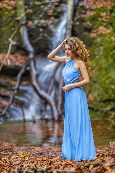 Eine schöne Frau im blauen Kleid in der Nähe eines Wasserfalls an einem Herbsttag — Stockfoto