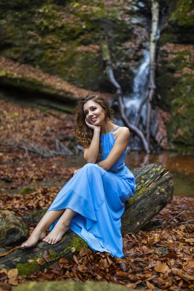 Piękna kobieta w niebieskiej sukience w pobliżu wodospadu w jesienny dzień — Zdjęcie stockowe
