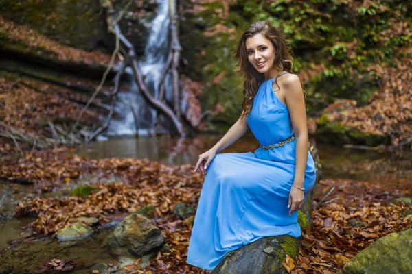Eine schöne Frau im blauen Kleid in der Nähe eines Wasserfalls an einem Herbsttag — Stockfoto