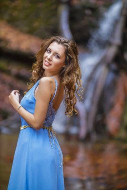 Sonbahar günü şelalenin yanında mavi elbiseli güzel bir kadın.
