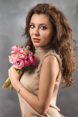 Gri arka planda güzel profesyonel makyajlı ve çiçekli genç bir kadının portresi.