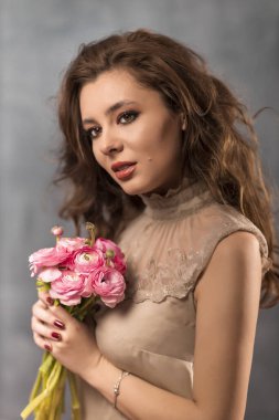 Gri arka planda güzel profesyonel makyajlı ve çiçekli genç bir kadının portresi.