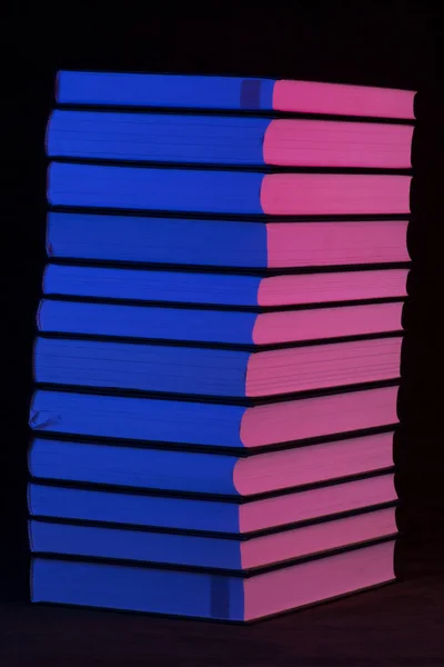 En trave böcker i rosa och blått ljus på en svart bakgrund — Stockfoto