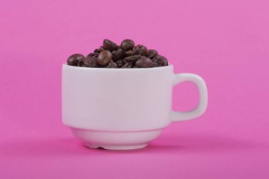 Kahve çekirdekleri pembe bir arka plan üzerinde beyaz fincan