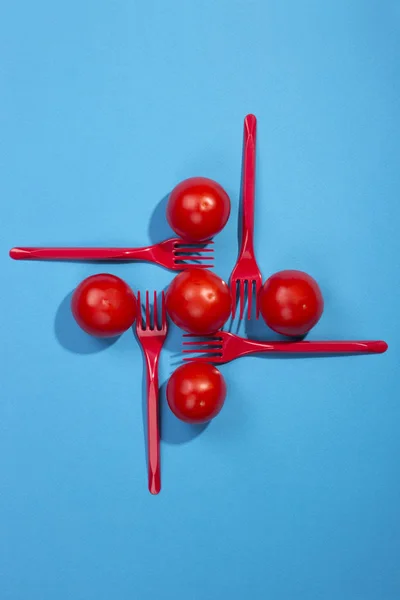 Bodegón abstracto con tomates y tenedores sobre fondo azul — Foto de Stock