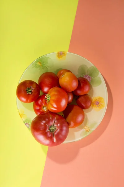 Naturaleza muerta abstracta con tomates en un plato sobre un fondo amarillo-rosado —  Fotos de Stock