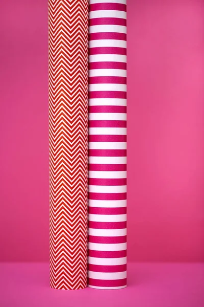 Paper rolls of colored paper on a pink background.