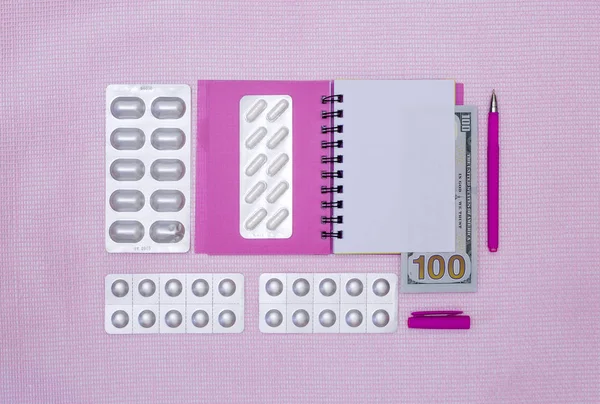 Notepad, pills and money on a pink background