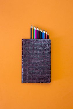 Defter ile renkli kalemler turuncu bir arka plan, üstten görünüm üzerinde bir dizi kapalı