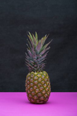 Olgun ananas meyvesi pembe bir masada koyu bir arka planda.