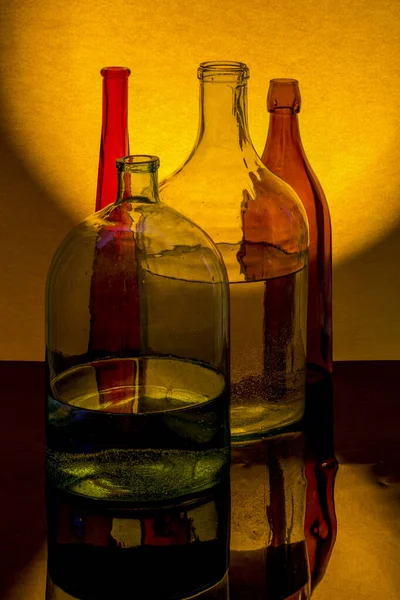黄色の背景に色のついたガラス製品で静物画 — ストック写真