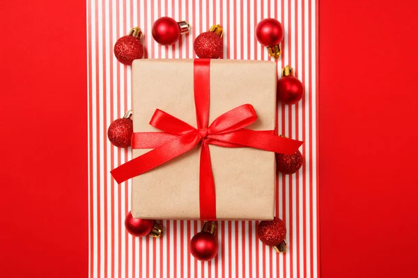 Bolas de brillo rojo navideño y regalo de papel artesanal sobre fondo rojo. Vista superior, plano . —  Fotos de Stock