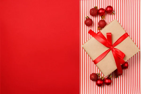 Bolas de brillo rojo navideño y regalo de papel artesanal sobre fondo rojo. Vista superior, plano, espacio para copiar . —  Fotos de Stock