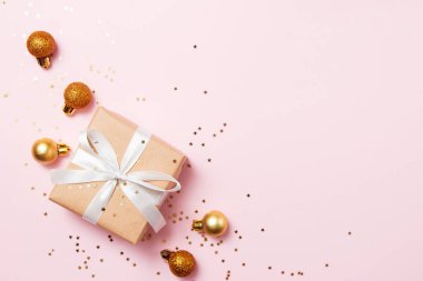 Noel tebrik kartı kompozisyonu. Pembe arka planda beyaz kurdeleli el işi kağıt hediye. Altın toplar ve konfeti yıldızı. Düz konum, üst görünüm, kopyalama alanı, moda biçimi.