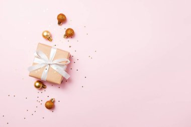 Noel tebrik kartı kompozisyonu. Pembe arka planda beyaz kurdeleli el işi kağıt hediye. Altın toplar ve konfeti yıldızı. Düz konum, üst görünüm, kopyalama alanı, moda biçimi.