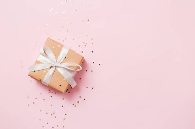 Noel kompozisyon tebrik kartı. Pembe arka planda altın yıldızlı bir konfetili el işi kağıdından hediye. Üst manzara, düz uzanma.