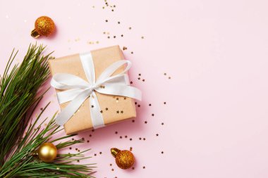 Noel tebrik kartı kompozisyonu. Beyaz kurdeleli kağıt hediye. Pembe arka planda. Noel ağacı, altın toplar ve konfeti yıldızı. Düz yatış, üst görünüm, moda tarzı.