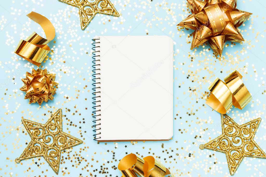 Clean notebook for goals or christmas shop list and resolutions on blue background with golden decorative stars and confetti. Top view, flat lay, copy space.