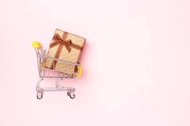 Üzerinde pembe pastel arka plan manzaralı hediye paketi olan Noel alışveriş arabası. Düzleştirme biçimi