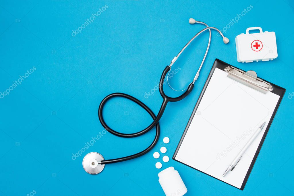 Top view of blank paper for writing doctor prescription with stethoscope. Pills on blue background. Health care concept. Top view, flat lay, copy space.