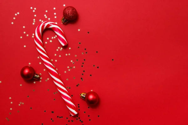 Composición navideña. Caramelo con confeti estrella y bolas sobre fondo rojo. Invierno, concepto de año nuevo. Plano, vista superior, espacio para copiar . —  Fotos de Stock