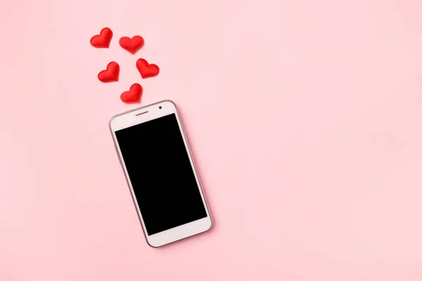 Top view of mobile cellphone and red heart on pink pastel background, copy space. Mockup template for Valentines Day. Love, technology concept. Top view, flat lay.