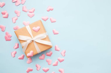 Mavi arka planda pembe kalp konfetisiyle beyaz fiyonklu mevcut. Düz yatış stili. Sevgililer Günü konsepti