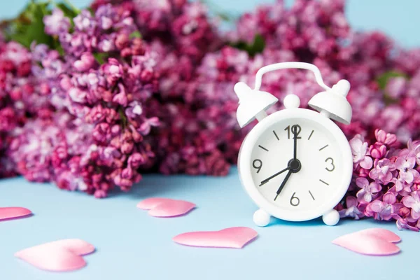 青い背景にヴィンテージ小さな目覚まし時計とライラックの花。春の朝のコンセプト. — ストック写真