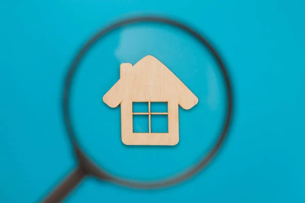 Lupa mirando una pequeña casa de madera sobre un fondo azul. Hipoteca y crédito para la compra. Concepto de bienes raíces, compra de vivienda asequible, alquiler de bienes raíces. Vista superior, plano —  Fotos de Stock