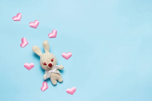 Amigurumi juguete de conejo de punto con corazones confeti sobre un fondo azul. Vista superior . — Foto de Stock