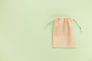 Asma ipli bez çanta, doğal pamuk kumaştan yapılmış küçük eko çuvalın maketi üst görünümden yeşil pastel arka planda yatıyordu.