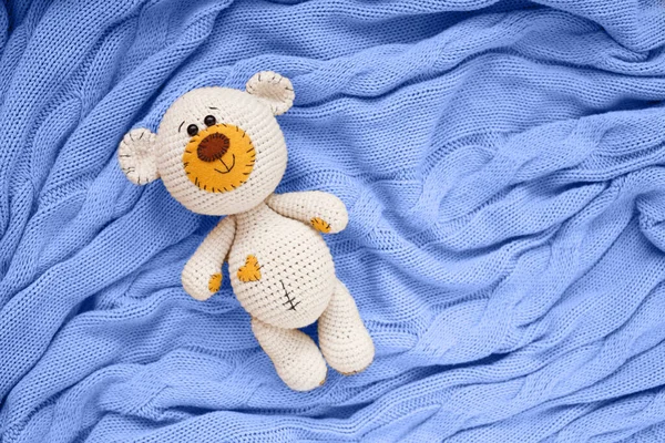 Un pequeño amigurumi de punto bebé oso de juguete está en una manta azul, la puesta plana, vista superior — Foto de Stock