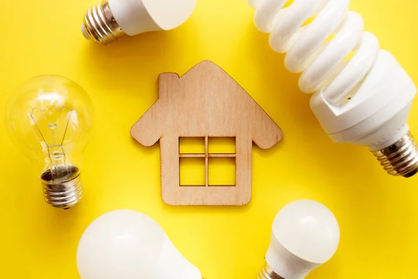 Lámpara led, fluorescente e incandescente con casa de madera sobre fondo amarillo. Vista superior, cama plana. Concepto de elección —  Fotos de Stock