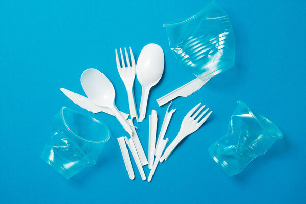 White single-use plastic knives, spoons, forks on a blue background. Say no to single use plastic. Environmental, pollution concept.