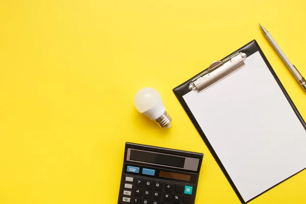 Blanco con una calculadora y una lámpara led económica sobre un fondo amarillo. Concepto de ahorro de luz eléctrica. Vista superior, plano . —  Fotos de Stock