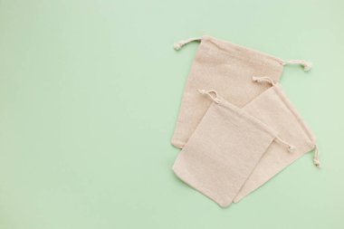 Asma ipli çantalar, doğal pamuk kumaştan yapılmış küçük eko çuvalların maketi, yukarıdan bakıldığında yeşil pastel arka planda yatıyordu.